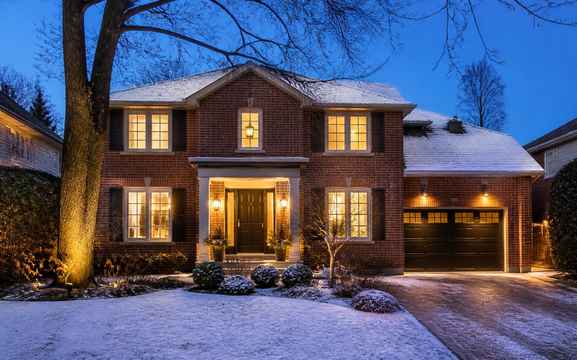 A warmly lit traditional brick two-storey Toronto family home on a winter evening